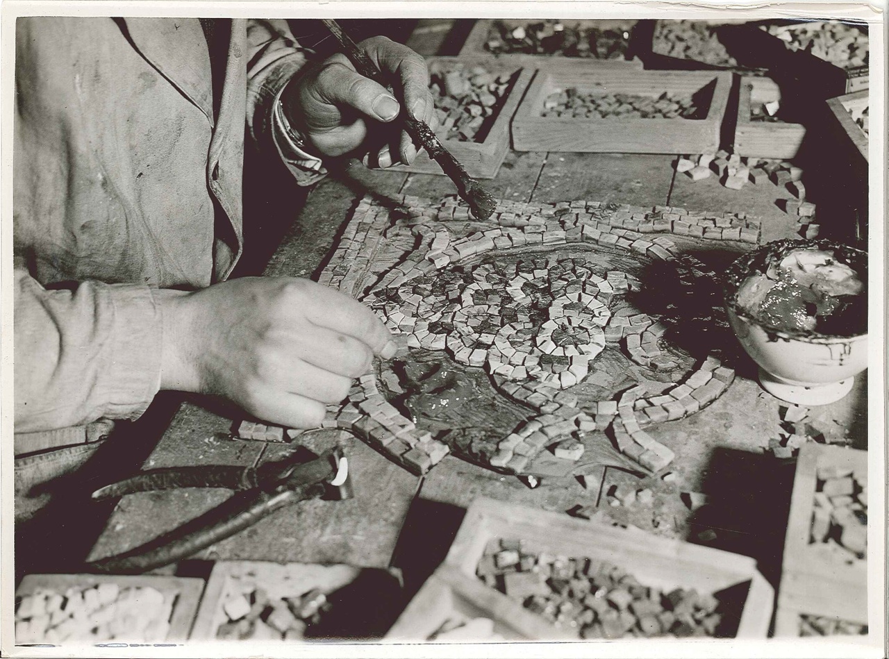 Foto uit de Cuypers' Kunstwerkplaatsen van rond 1930: het opplakken van een mozaïeksteentje, nadat het de gewenste vorm heeft verkregen.