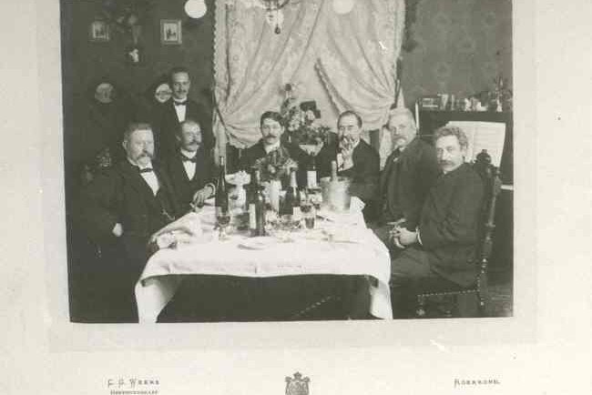 Groepsfoto van de heer J. Janssen en andere heren aan feestelijk gedekte tafel