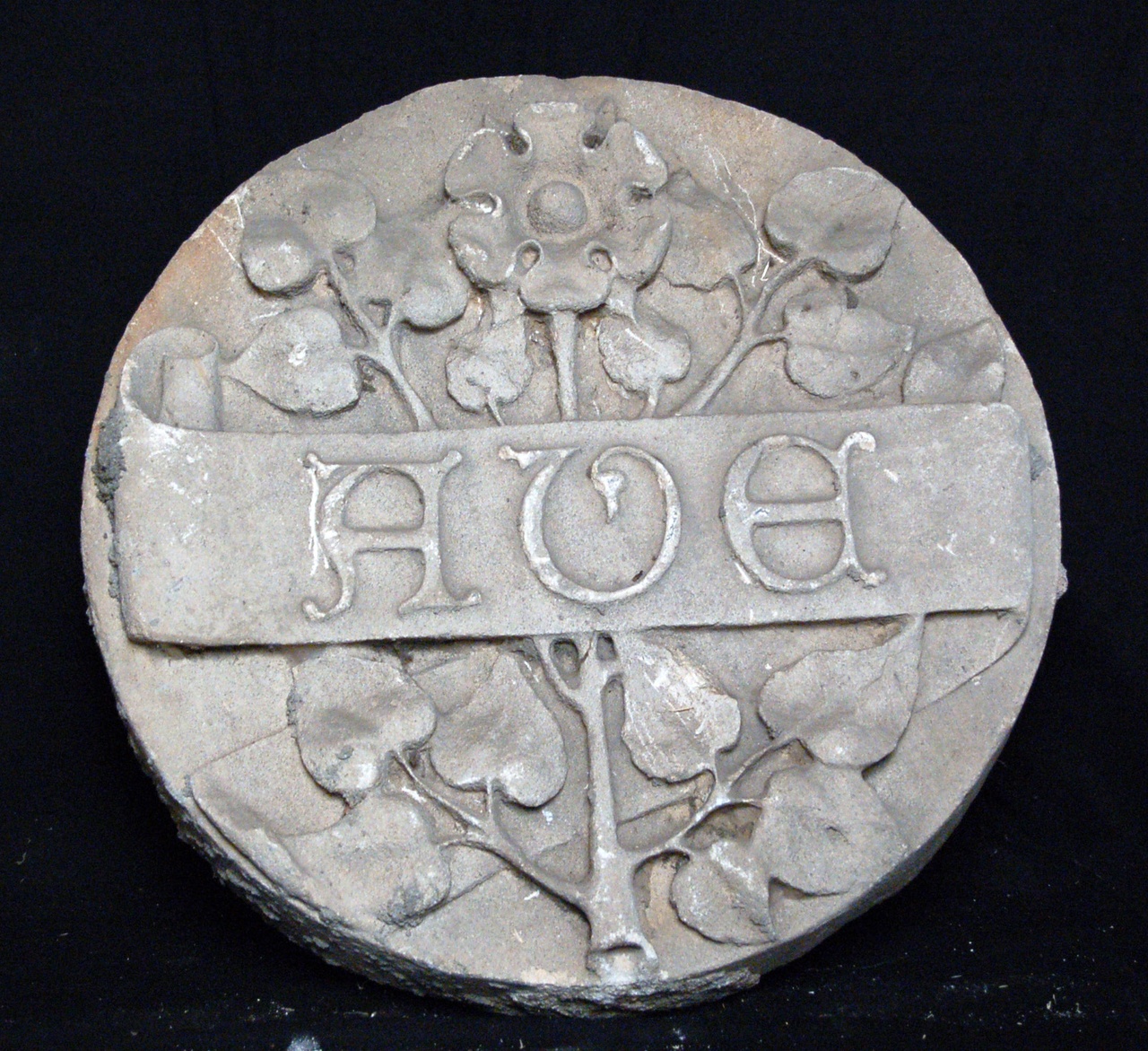 Cirkelvormige platte steen met de tekst 'AVE' in banderole