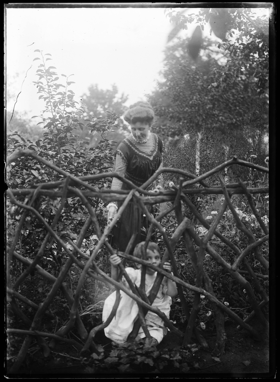 Glasnegatief van een foto van Delphine Cuypers-Povel met Charles Cuypers in de tuin achter een houten hekwerk