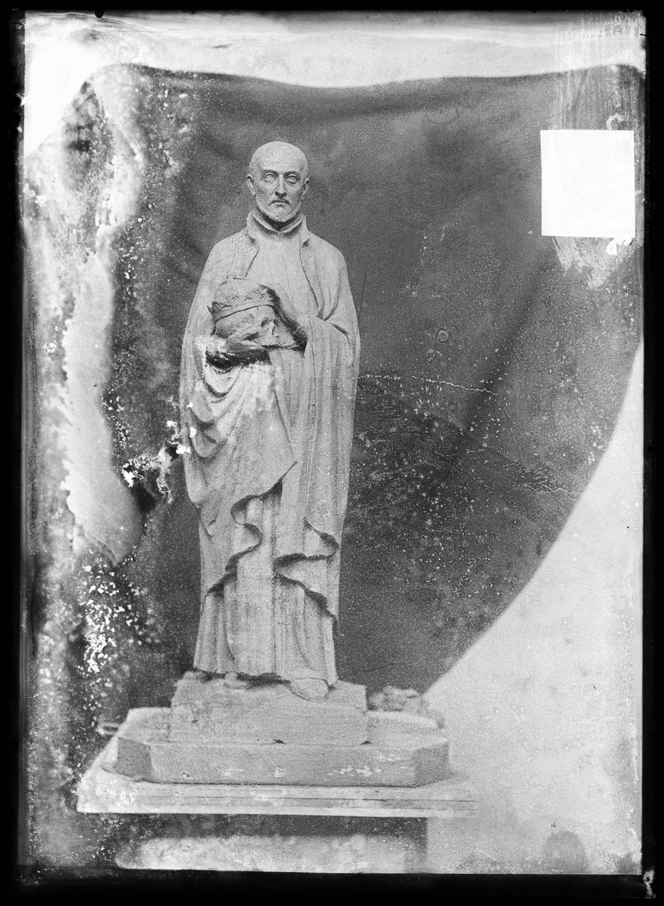 Glasnegatief van foto van producten uit de Cuypers' Kunstwerkplaatsen: "Foto van een beeld van een monnik of priester met een gekroond doodshoofd in zijn hand".