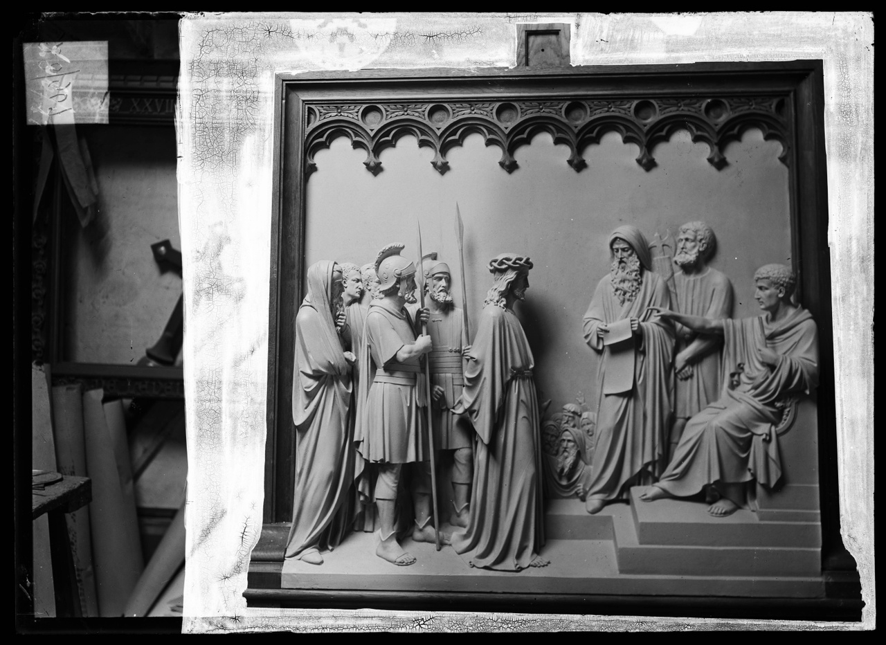 Glasnegatief van foto van producten uit de Cuypers' Kunstwerkplaatsen: "Foto van een houten sierlijst met daarin een reliëf van een kruiswegstatie: de veroordeling van Christus door Pontius Pilatus ".