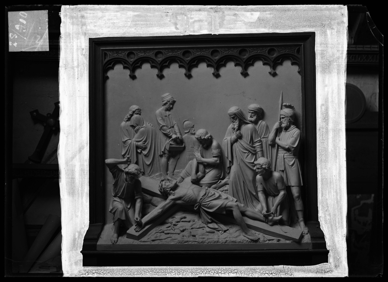 Glasnegatief van foto van producten uit de Cuypers' Kunstwerkplaatsen: "Foto van een houten sierlijst waarbinnen een kruiswegstatie: Jezus wordt aan het kruis genageld en gebonden".