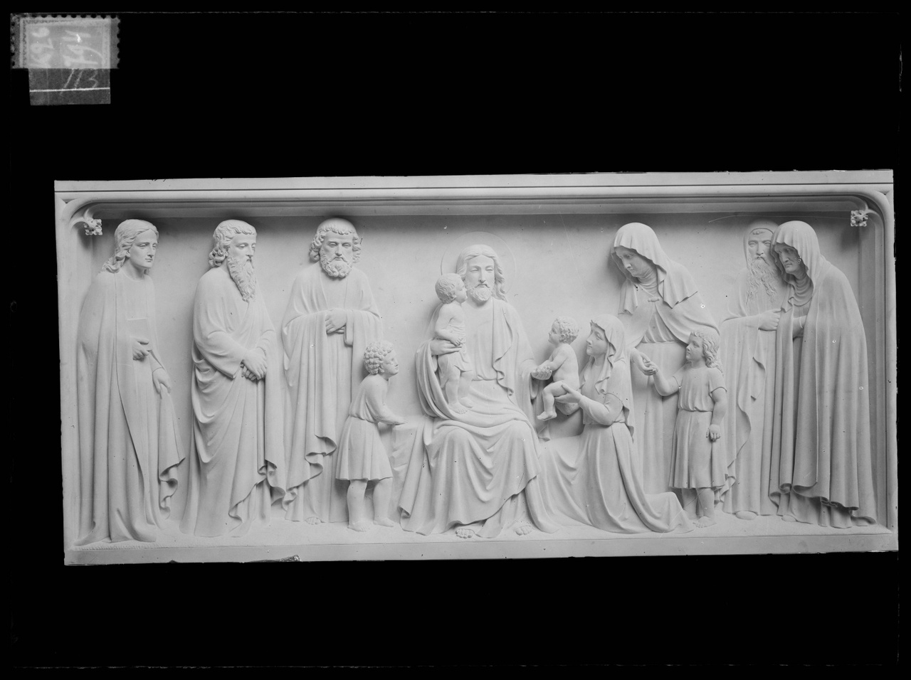Glasnegatief van foto van producten uit de Cuypers' Kunstwerkplaatsen: "Foto van een gipspaneel met daarop Christus met vier kinderen omringd door enkele mannen en vrouwen.".